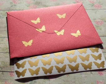 Puede incluir: Una hoja de pegatinas de mariposas doradas sobre un fondo blanco. La hoja está encima de un sobre rojo con pegatinas de mariposas doradas.