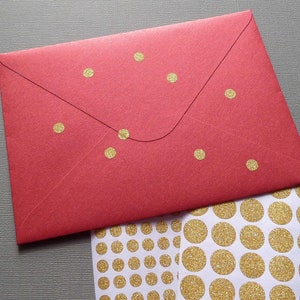 May include: A red envelope with gold glitter dot stickers. The envelope has a flap closure and gold dots scattered across the front. A sheet of gold glitter dot stickers is next to the envelope.