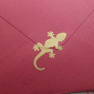 May include: A red envelope with a gold lizard-shaped embellishment. The envelope is sealed and has a simple, elegant design. The lizard is a decorative element, adding a touch of nature-inspired charm to the stationery.