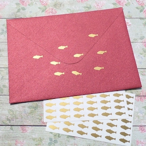 May include: A red envelope with gold fish stickers. A sheet of white paper with gold fish stickers is below the envelope.