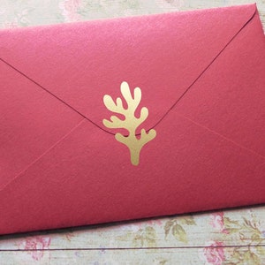 Könnte beinhalten: Ein roter Umschlag mit einer goldenen, korallenförmigen Verzierung. Der Umschlag ist verschlossen und hat eine strukturierte Oberfläche. Der Hintergrund ist eine Holzoberfläche mit floralem Muster.
