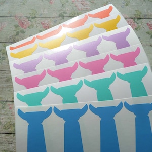 Könnte beinhalten: Ein Stapel weißer Blätter mit bunten, ausgestanzten Aufklebern eines Comic-Charakters. Die Aufkleber sind in verschiedenen Farben, darunter Pink, Blau, Gelb, Orange und Lila. Der Charakter hat einen großen Kopf, einen kleinen Körper und große Ohren.