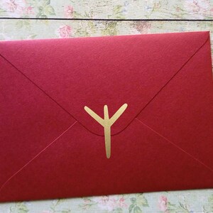 Könnte beinhalten: Ein roter Umschlag mit einem goldenen Y-förmigen Design in der Mitte.