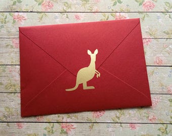 May include: A red envelope with a gold kangaroo silhouette. The envelope is rectangular and sealed, with the kangaroo emblem centered on the front. The background is a floral pattern.