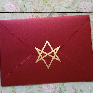 May include: A red envelope with a gold geometric star design. The envelope is closed and has a textured surface. The background is a floral pattern on a wooden surface.