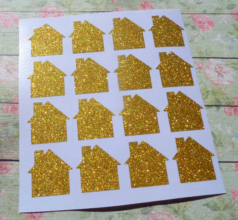 May include: A sheet of gold glitter house stickers. There are 16 stickers in total, arranged in a 4x4 grid.