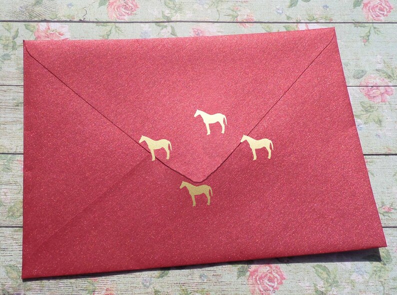 May include: Red envelope with four gold horse silhouettes. The envelope is textured and has a glitter finish.