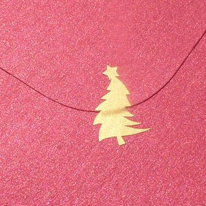 Könnte beinhalten: Ein festlicher, pinkfarbener Umschlag mit einem goldenen Weihnachtsbaum-Ausschnitt und Stern. Der Umschlag hat eine glitzernde Textur und einen dünnen, dunklen Faden. Das Design hat ein festliches Thema.