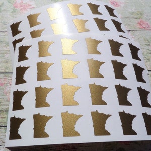 May include: A sheet of gold foil stickers featuring the outline of the state of Minnesota. There are 36 stickers on the sheet.