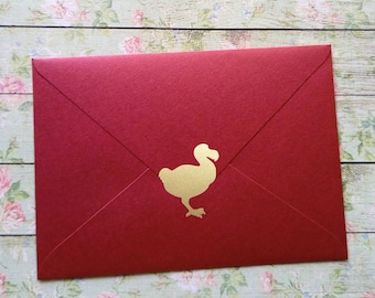 Pode incluir: Um envelope vermelho com uma silhueta dourada de um dodô.