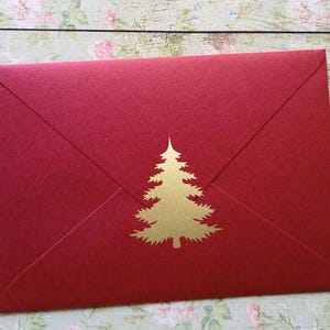 Può includere: Una busta rossa con un disegno di albero di Natale dorato. La busta è rettangolare con un lembo a punta ed è realizzata in carta strutturata. L'albero dorato è centrato sul davanti.