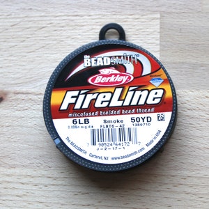 Könnte beinhalten: Eine Spule Berkley FireLine mikrofusionierter geflochtener Perlenschnur, 6 lb Test, in der Farbe Smoke. Die Spule ist schwarz und rot mit weißen Buchstaben und enthält 45,72 Meter Faden. Die Verpackung enthält den Text "The BEADSMITH" und "Made in USA".