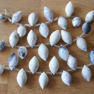 May include: A strand of white and grey teardrop-shaped gemstone beads with silver accents. The beads are strung on a clear thread and are arranged in a loose, flowing pattern.