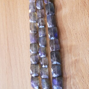 May include: A strand of faceted labradorite beads in shades of grey and blue. The beads are square shaped and have a polished finish.