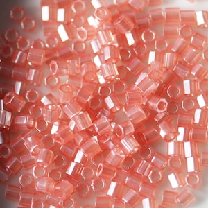 May include: A close-up of a pile of small, translucent, hexagonal beads in a light pink colour. The beads have a slight iridescent sheen.