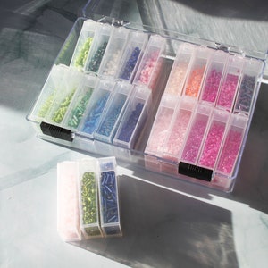 May include: A clear plastic storage box filled with small containers of colourful beads. The containers are arranged in rows and columns. The beads are a variety of colours, including pink, green, blue, and white.