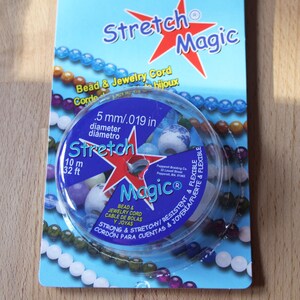Könnte beinhalten: Eine Spule aus klarem, elastischem Stretch-Magic-Perlen- und Schmuckband. Die Spule ist mit dem Text "Stretch Magic" und "Bead & Jewelry Cord" beschriftet. Die Spule ist 10 Meter oder 32 Fuß lang und hat einen Durchmesser von 0,5 mm oder 0,019 Zoll.