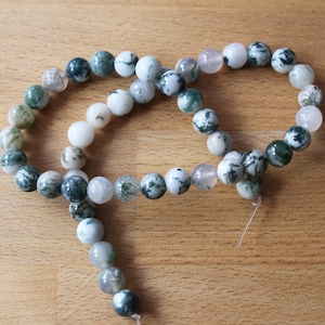 May include: A strand of green and white agate beads, with some beads having a translucent white colour. The beads are strung on a clear elastic cord.
