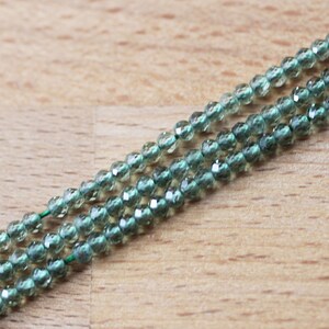 May include: A strand of green faceted glass beads. The beads are small and round, and they are strung on a clear thread.