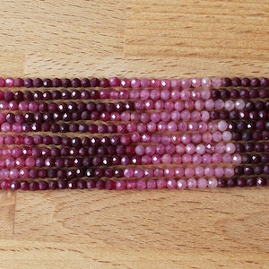 Könnte beinhalten: Eine Strähne facettierter Edelsteinperlen in Rosatönen und Violett. Die Perlen sind rund und haben eine glatte, polierte Oberfläche.