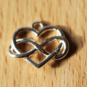 May include: Silver charm in the shape of a heart with an infinity knot design.