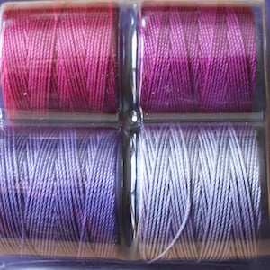May include: Four spools of embroidery floss, two are a gradient of pink and purple, and two are a gradient of white and purple.