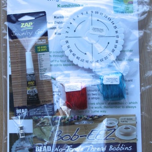May include: A Kumihimo starter kit containing a white Kumihimo disc, eight white Bob-EEZ No-Tangle Thread Bobbins, a pack of eight magnetic clasps, a bottle of Zap Gel glue, two spools of shiny synthetic thread, and instructions. The kit is packaged in a clear plastic bag.