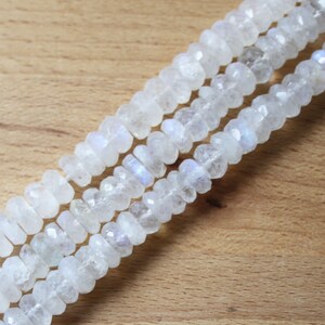 May include: A strand of white moonstone beads with a faceted, elongated, rectangular shape. The beads have a subtle iridescent shimmer.