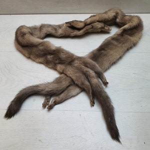 Op de afbeelding: Een bruine bonten sjaal gemaakt van meerdere wezelstaarten. De sjaal is in een losse knoop geknoopt en de staarten hangen naar beneden.
