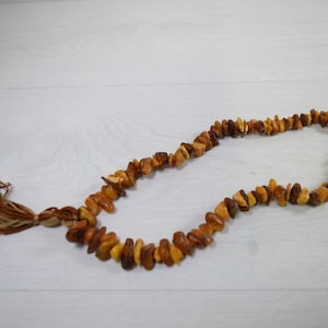 May include: A brown amber necklace with a tassel made of brown and beige string.