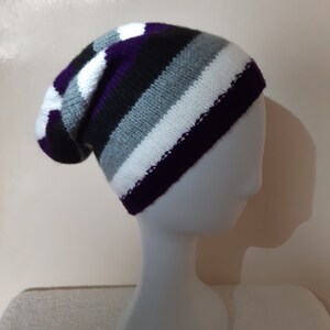 May include: A black, white, gray, and purple striped knitted beanie hat. The hat is slouchy and has a fold-over brim.