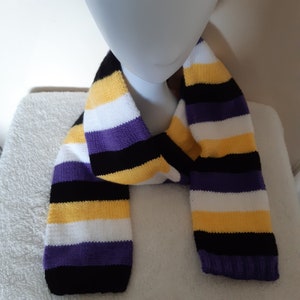 May include: A purple, white, yellow and black striped knitted scarf. The scarf is folded in half and draped over a mannequin's neck.