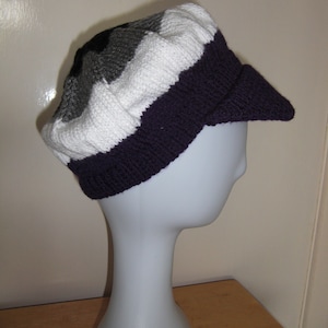 May include: A knitted hat with a visor in shades of gray, white, and purple. The hat is on a white mannequin head.