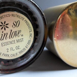 K&ouml;nnte beinhalten: Eine goldene Flasche mit einem schwarzen Etikett, auf dem steht "*SO in love* ESSENCE MIST 2 fl oz. EDITH REHNBERG COSMETICS - NUTRILITE PRODUCTS, INC. BUENA PARK, CALIF. 90620 87-095."