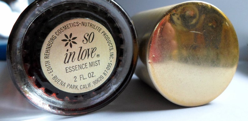 K&ouml;nnte beinhalten: Eine goldene Flasche mit einem schwarzen Etikett, auf dem steht "*SO in love* ESSENCE MIST 2 fl oz. EDITH REHNBERG COSMETICS - NUTRILITE PRODUCTS, INC. BUENA PARK, CALIF. 90620 87-095."