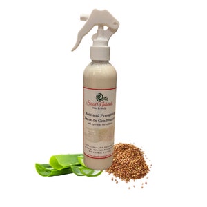 May include: A white bottle of "Sired Naturals Hair & Body Aloe and Fenugreek Leave-In Conditioner with Ayurvedic Herbs Blend" with a spray nozzle. The bottle is surrounded by green aloe vera leaves and brown fenugreek seeds.