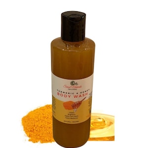 May include: A clear bottle of turmeric and honey body wash with a black cap. The bottle is labeled "Strad Naturals Hair & Body Turmeric & Honey Body Wash". The label also lists the benefits of the product: cleans, brightens, fades dark spots, clears back acne. The bottle is sitting on a white surface with a pile of turmeric powder and a pool of honey.