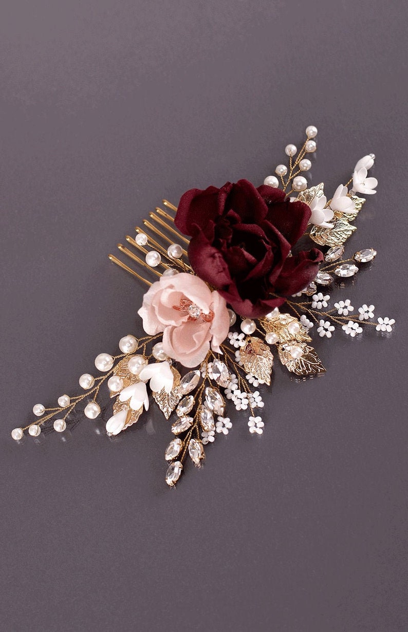 May include: A burgundy and blush floral hair comb with gold leaves, pearls, and rhinestones. The comb is ideal for weddings or special occasions.