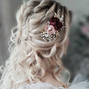 May include: A bridal hair comb featuring burgundy and blush pink fabric flowers, gold leaves, and crystal rhinestones.