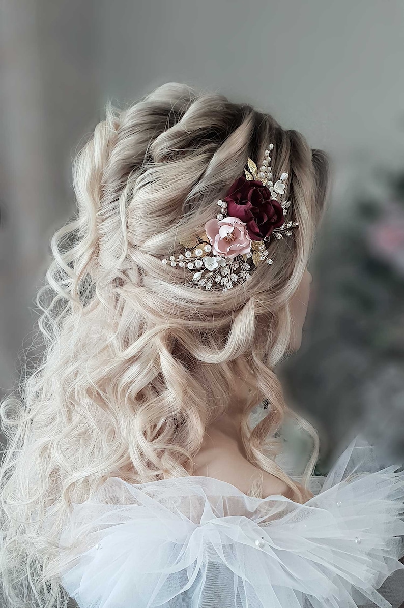 May include: A bridal hair comb featuring burgundy and blush pink fabric flowers, gold leaves, and crystal rhinestones.