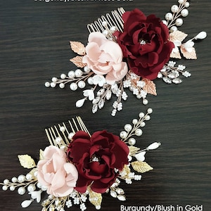May include: Two hair combs featuring burgundy and blush pink fabric flowers, gold leaves, and pearl and crystal embellishments. The top comb has rose gold accents and the bottom comb has gold accents. The text "Burgundy/Blush in RoseGold" is above the top comb and "Burgundy/Blush in Gold" is below the bottom comb.