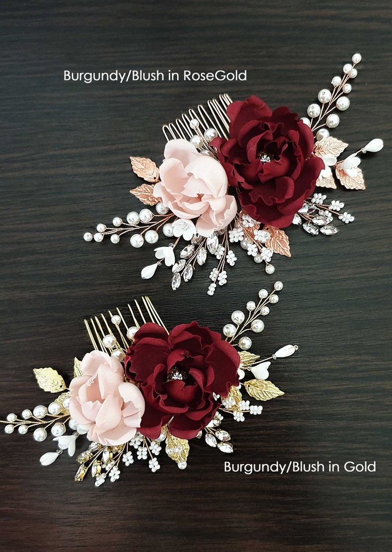 May include: Two hair combs featuring burgundy and blush pink fabric flowers, gold leaves, and pearl and crystal embellishments. The top comb has rose gold accents and the bottom comb has gold accents. The text "Burgundy/Blush in RoseGold" is above the top comb and "Burgundy/Blush in Gold" is below the bottom comb.