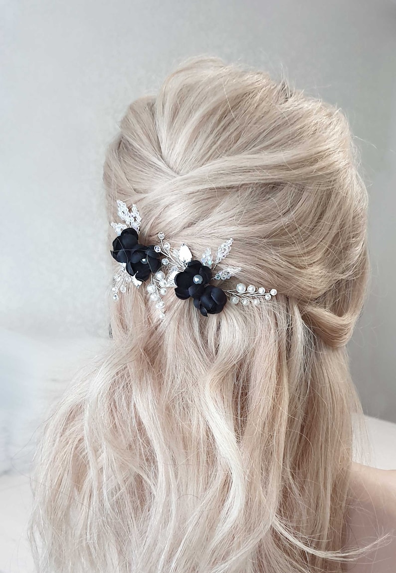 Puede incluir: Primer plano de un peinado rubio adornado con dos horquillas de flores negras. Las horquillas est&aacute;n adornadas con cristales y peque&ntilde;as cuentas blancas. El cabello est&aacute; peinado en un estilo semi recogido.