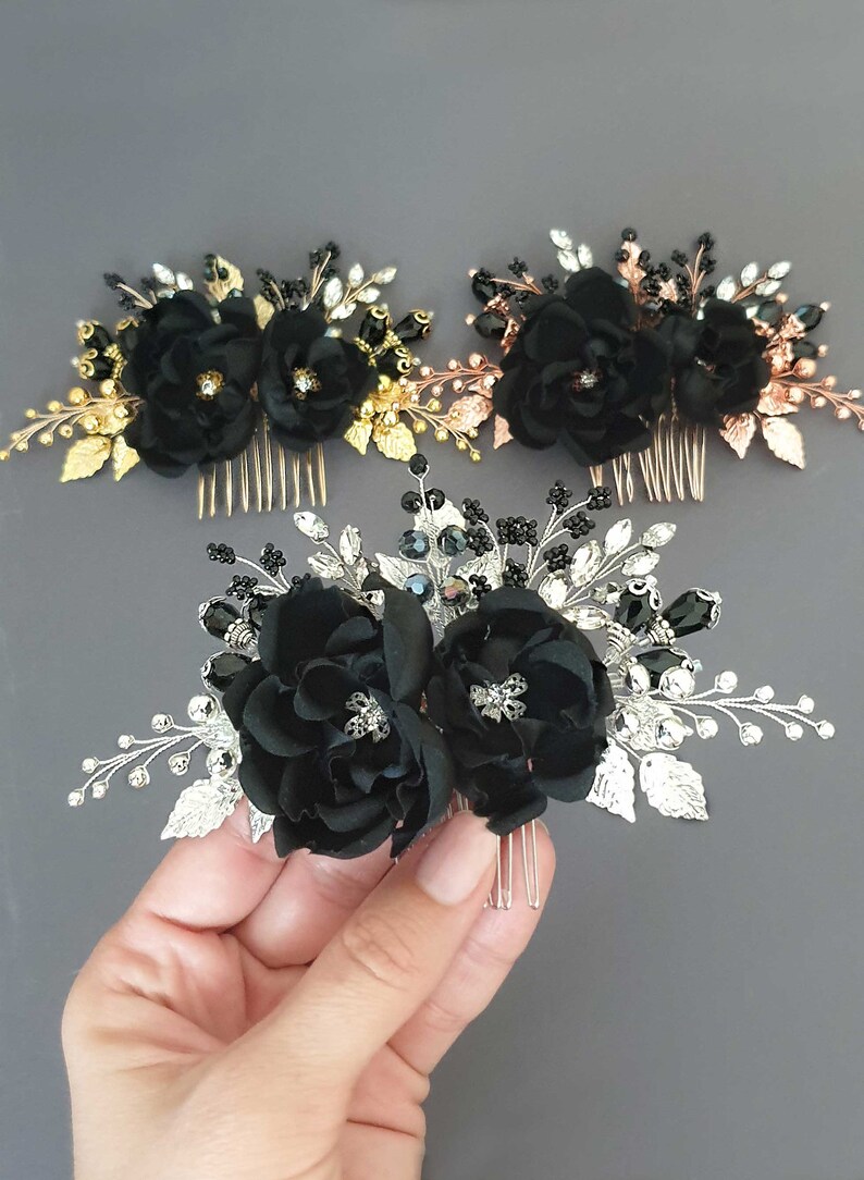 Puede incluir: Tres peinetas florales con flores de tela negra y detalles decorativos. Una peineta tiene hojas y detalles dorados, otra tiene oro rosa y la tercera tiene detalles plateados. Las peinetas est&aacute;n sobre un fondo gris.