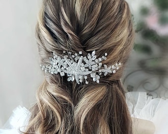 May include: A silver hair comb with a floral design and crystal embellishments. The comb is worn in a woman's hair, which is styled in a half-updo.