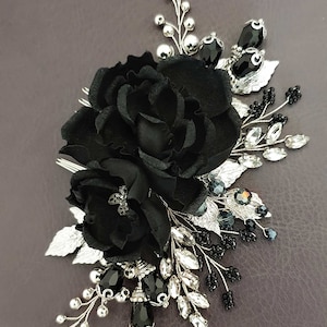 Puede incluir: Una horquilla floral negra con una gran flor de tela y flores de acento m&aacute;s peque&ntilde;as. La horquilla presenta hojas plateadas, cristales transparentes y negros y peque&ntilde;as cuentas negras. Un accesorio elegante para ocasiones especiales.