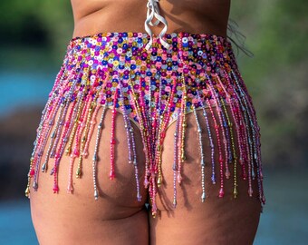 May include: A sequined and beaded skirt with a fringe bottom in shades of pink, purple, and gold. The skirt is worn low on the hips and has a white string tie at the waist.