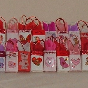 May include: A collection of small, colorful gift bags with various Valentine's Day themes. The bags are decorated with hearts, flowers, and other romantic designs. Some bags have small teddy bears or other cute characters.