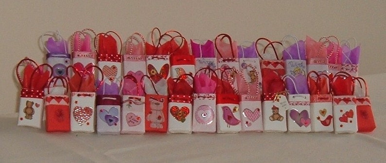 May include: A collection of small, colorful gift bags with various Valentine's Day themes. The bags are decorated with hearts, flowers, and other romantic designs. Some bags have small teddy bears or other cute characters.