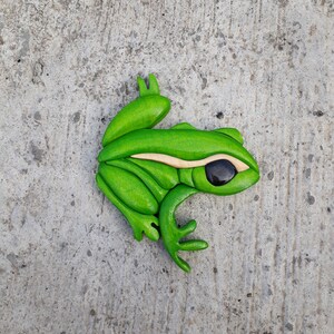 May include: A green wooden frog sculpture with black eyes. The frog is carved in a realistic style and has a detailed texture.
